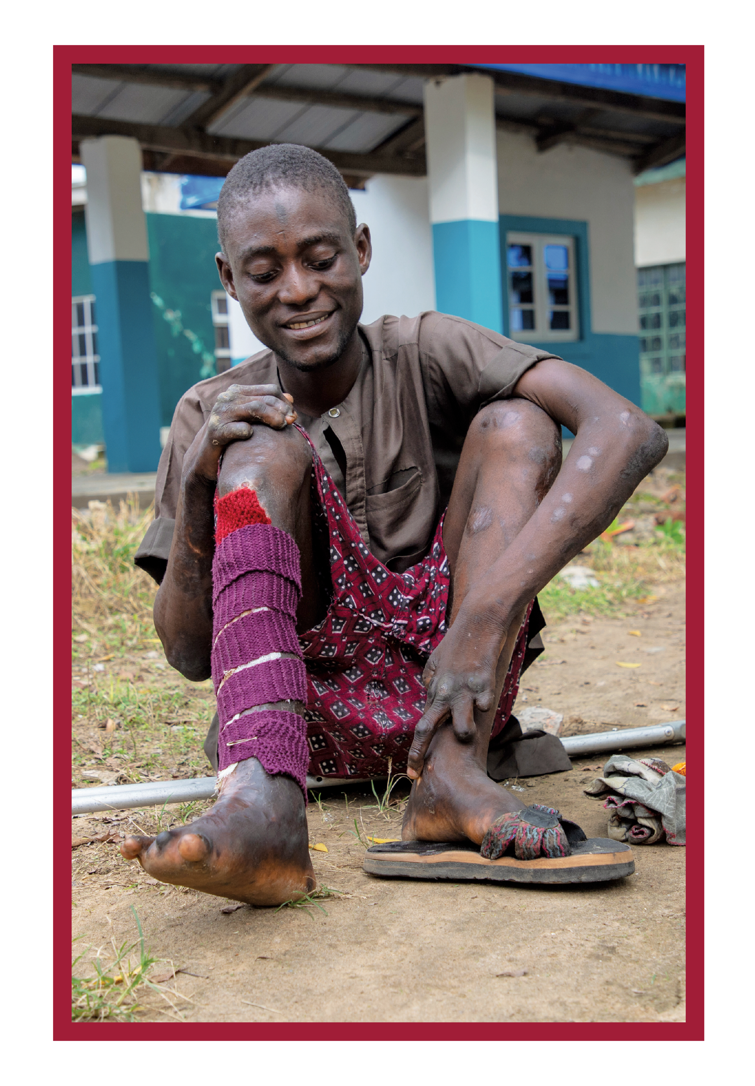 Abubakar sitting on the ground, smiling as he looks at a pair of protective shoes.